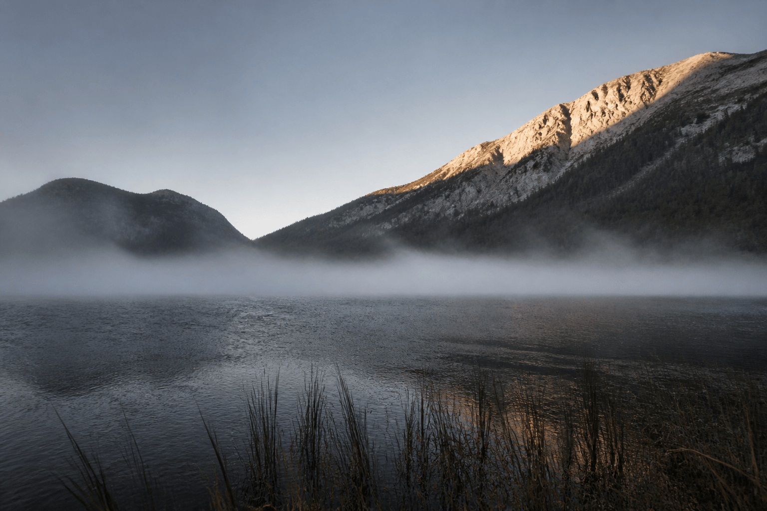 Mist resting on a dark alpine lake at first light.