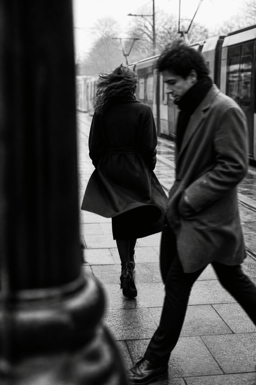 Two strangers passing beside a tram on a wet winter day.
